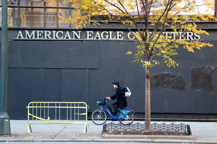 A person on a CitiBike cycles by a boarded up American Eagle Outfitters store